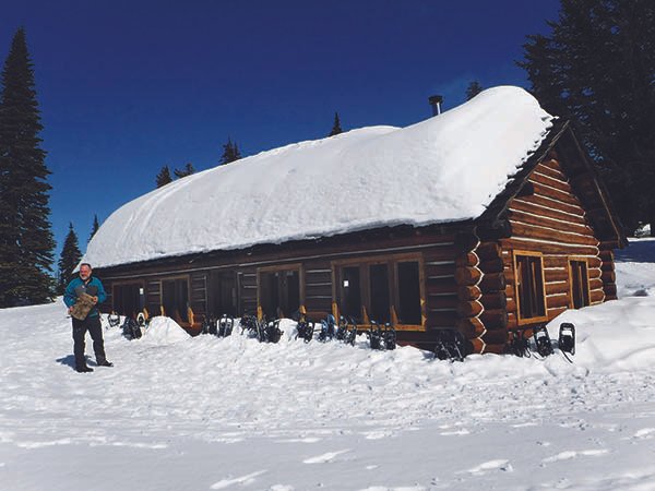 Person snowshoeing standing next to a CCC cabin at Mount Spokane State Park.