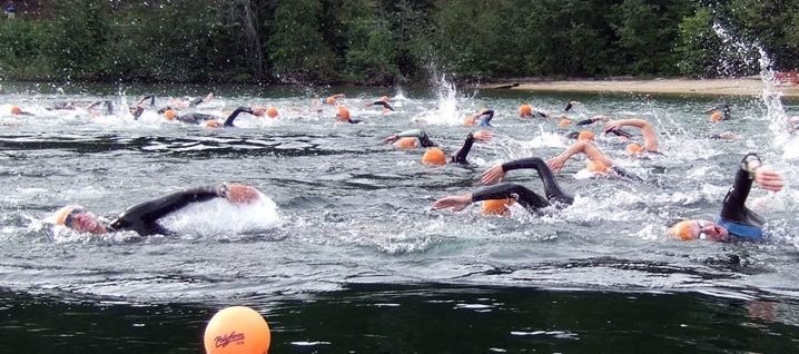 Swim racers in black wetsuits and red swim caps freestyle swimming during the Priest Lake Triathlon.