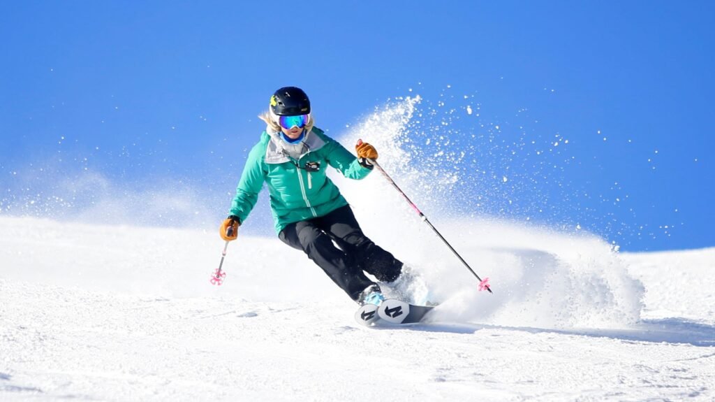 Woman wearing green jacket and black ski pants skis parallel turns down a groomed run at Silver Mountain on a sunny, blue sky day.