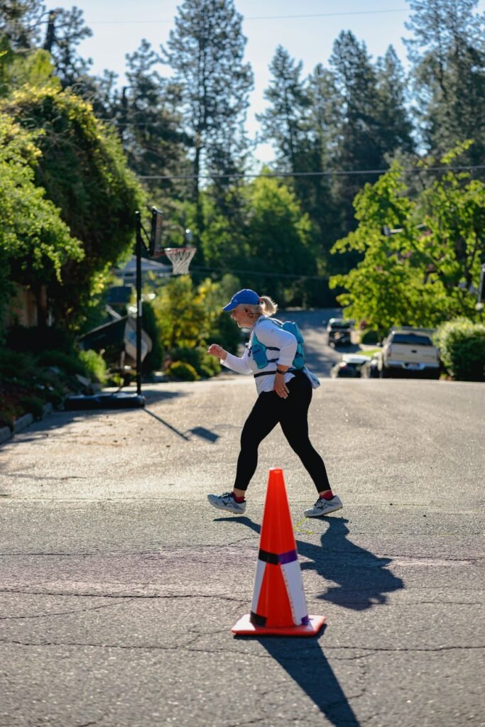 Woman walking along Coeur d'Alene Marathon course near an orange traffic cone.