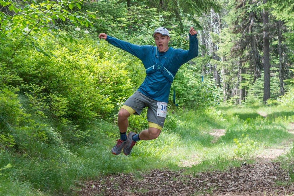 Male runner gleefully running and jumping along a dirt trail at Mt Spokane State Park during the Mountain Magic Trail Run event.