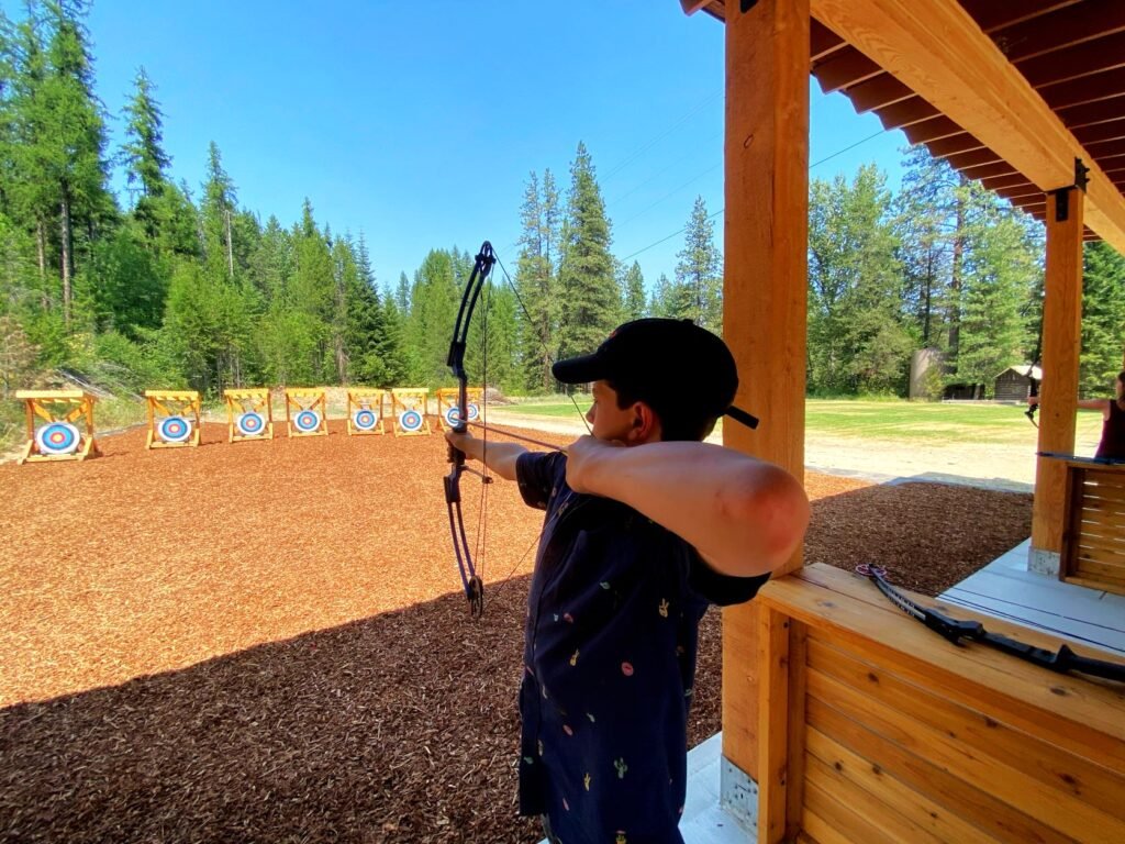 Camper at archery range at Camp Spalding--holding the bow and stretching back string with arrow, aiming at bullseye target.
