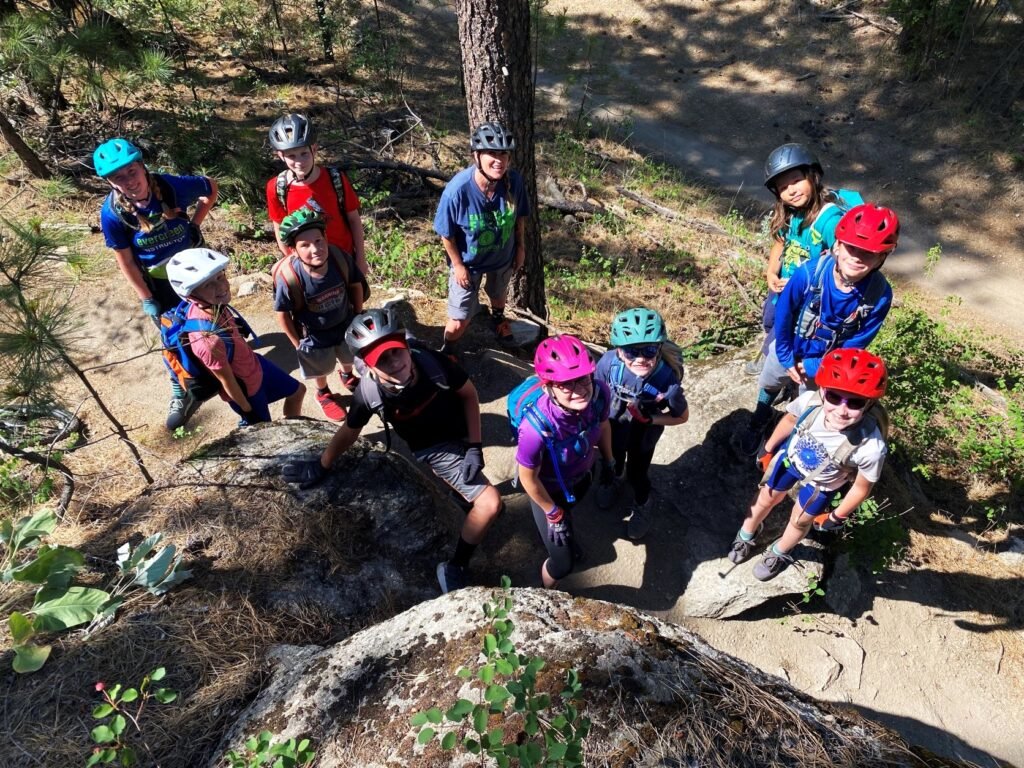 Evergreen East mountain bike campers taking a break for a photo--sitting on rock boulders, looking up, smiling at camera.