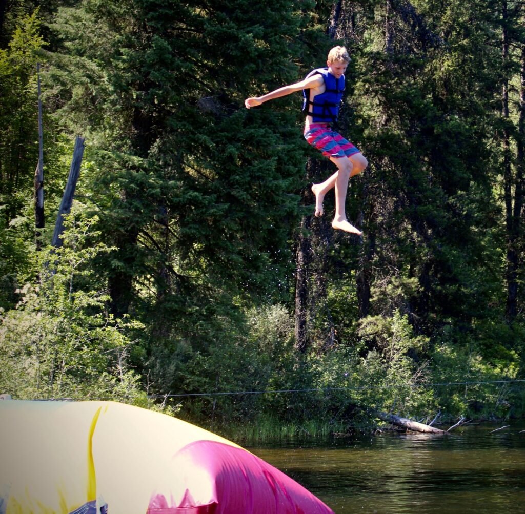 Teenager wearing a life-jacket in the air above the lake water after being launched off the inflatable "Blob" water toy.