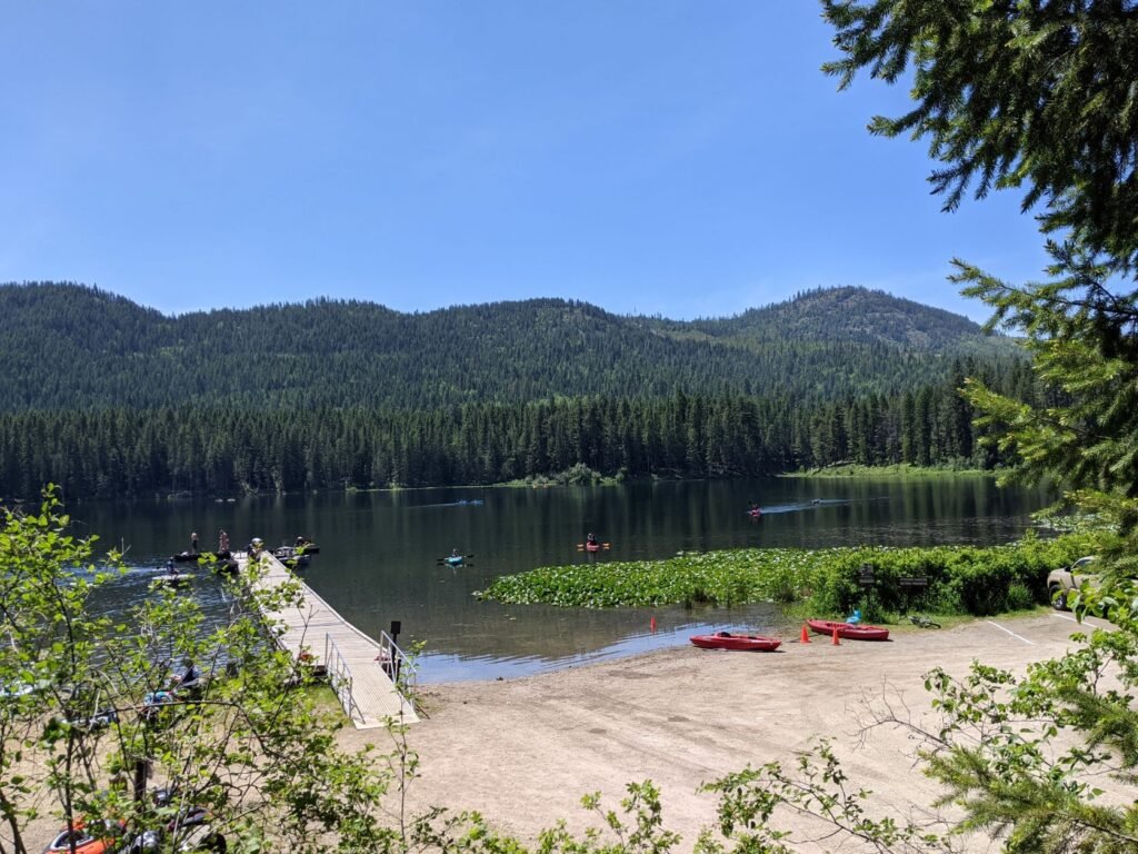 View of Round Lake and the day-use dock and boat launch near the beach, and hills rising from the opposite shore, with two red kayaks resting on the shore.
