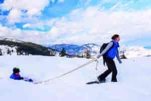Photo of skier pulling child in snow tube.