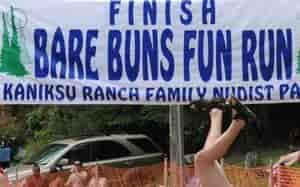 Large Finish Line banner that reads, "FINISH BARE BUNS FUN RUN - Kaniksu Ranch Family Nudist Park," with a view of people's heads and someone's legs and shoed-feet as if doing a handstand.