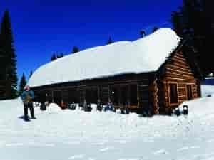Person snowshoeing standing next to a CCC cabin at Mount Spokane State Park.