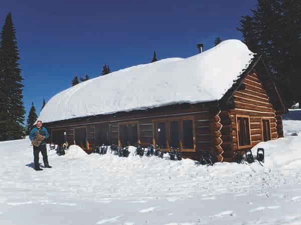 Person snowshoeing standing next to a CCC cabin at Mount Spokane State Park.