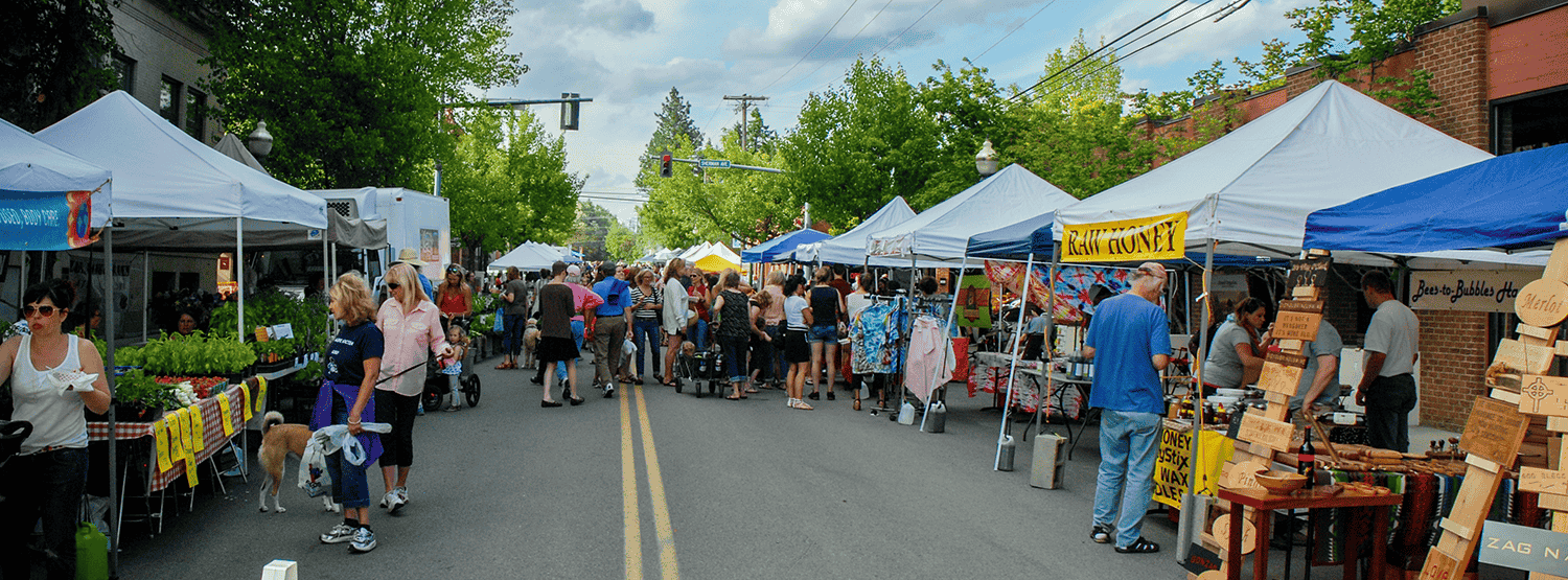 Photo of farmers market with people shopping at various stalls.