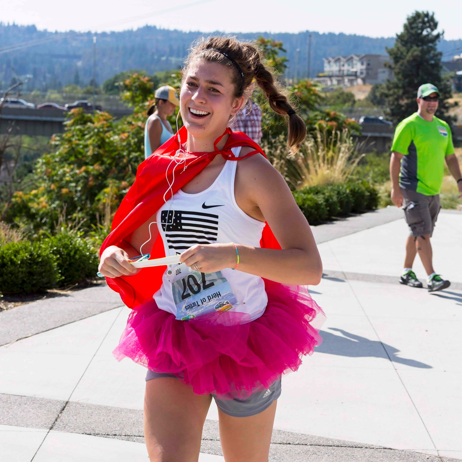 A spirited runner with tutu and cape holds the exchange bracelet for her team. 