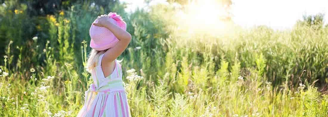 Little girl in sundress and hat in field.
