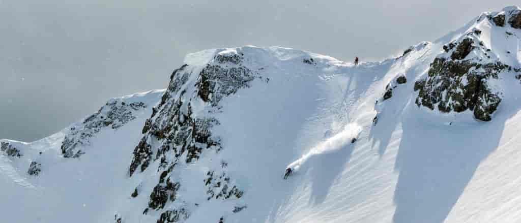 photo of backcountry skier on mountain peak from a distance.