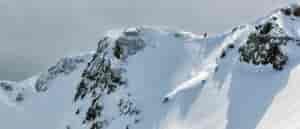 photo of backcountry skier on mountain peak from a distance.