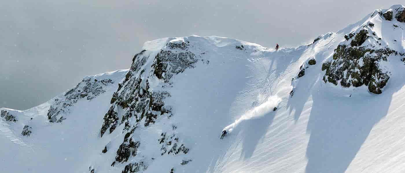 photo of backcountry skier on mountain peak from a distance.