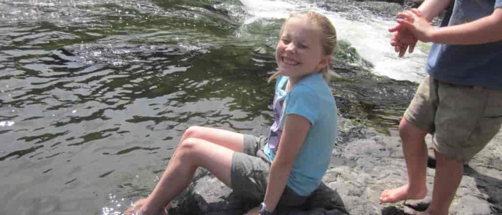 Photo of girl sitting on a rock with her feet in the water.