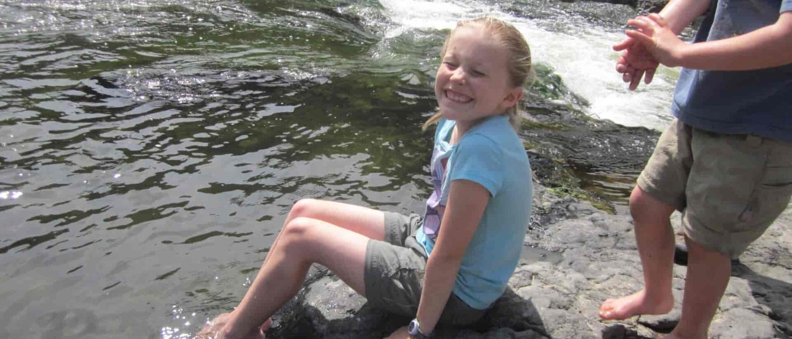 Photo of girl sitting on a rock with her feet in the water.