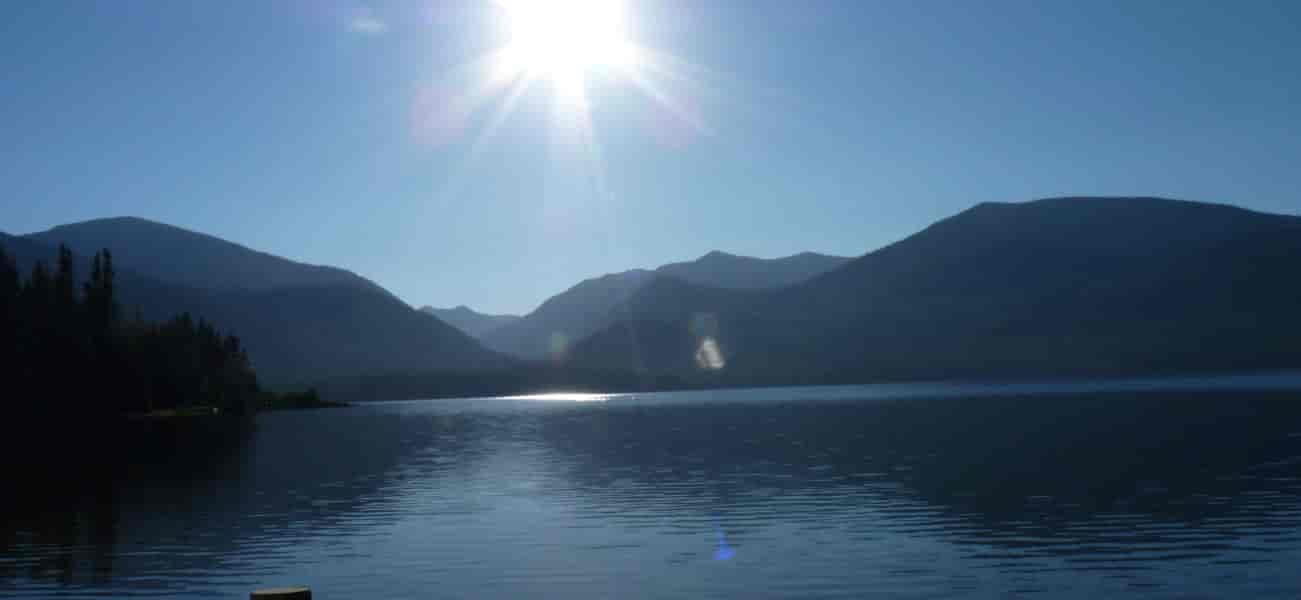 Still water of Priest Lake with mountain peaks and sun in the background.