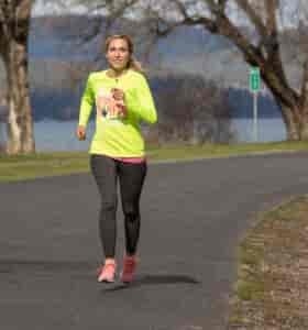 Woman running on the Centennial Trail in Spokane, with a few of trees and the Spokane River in the background.