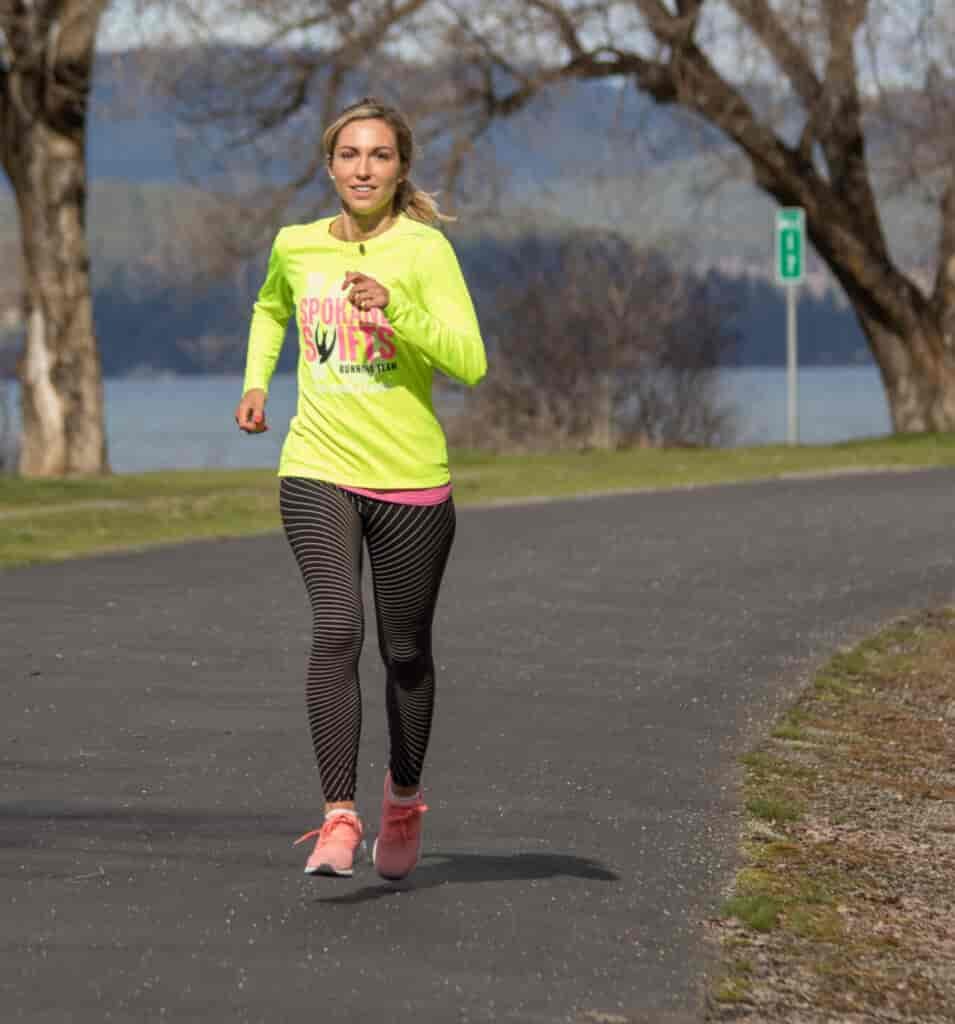 Woman running on the Centennial Trail in Spokane, with a few of trees and the Spokane River in the background.