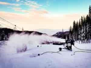 Snow-blowing machine shooting out new snow on a ski run.