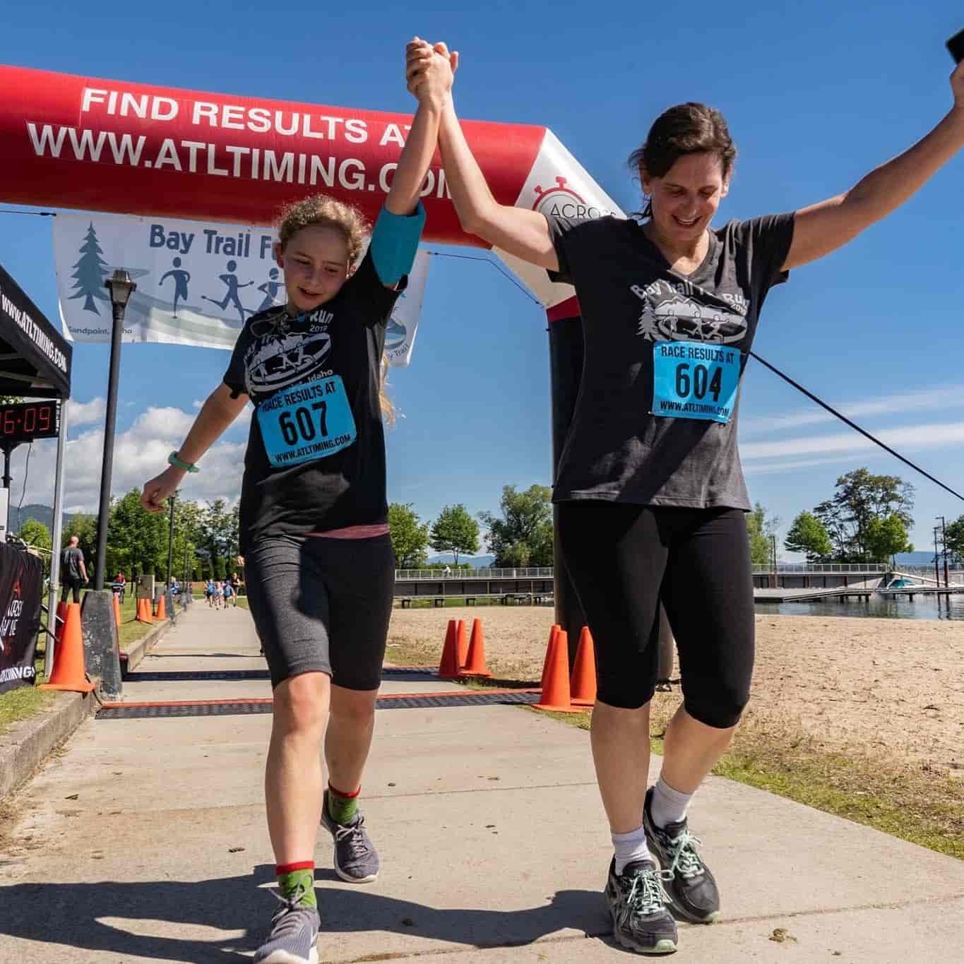 A mother and daughter crossing the finish line of a fun run.