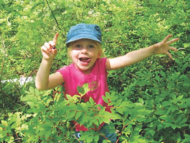 A kid smiling while collecting wild berries.