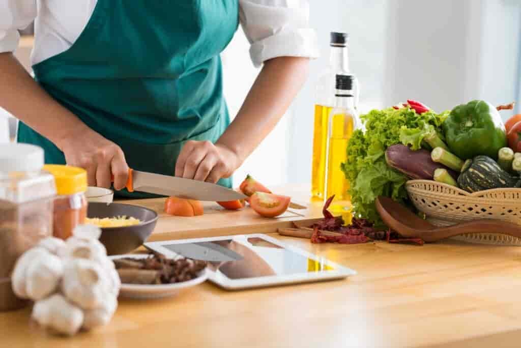 Person wearing an apron cutting vegetables with other cooking supplies nearby.