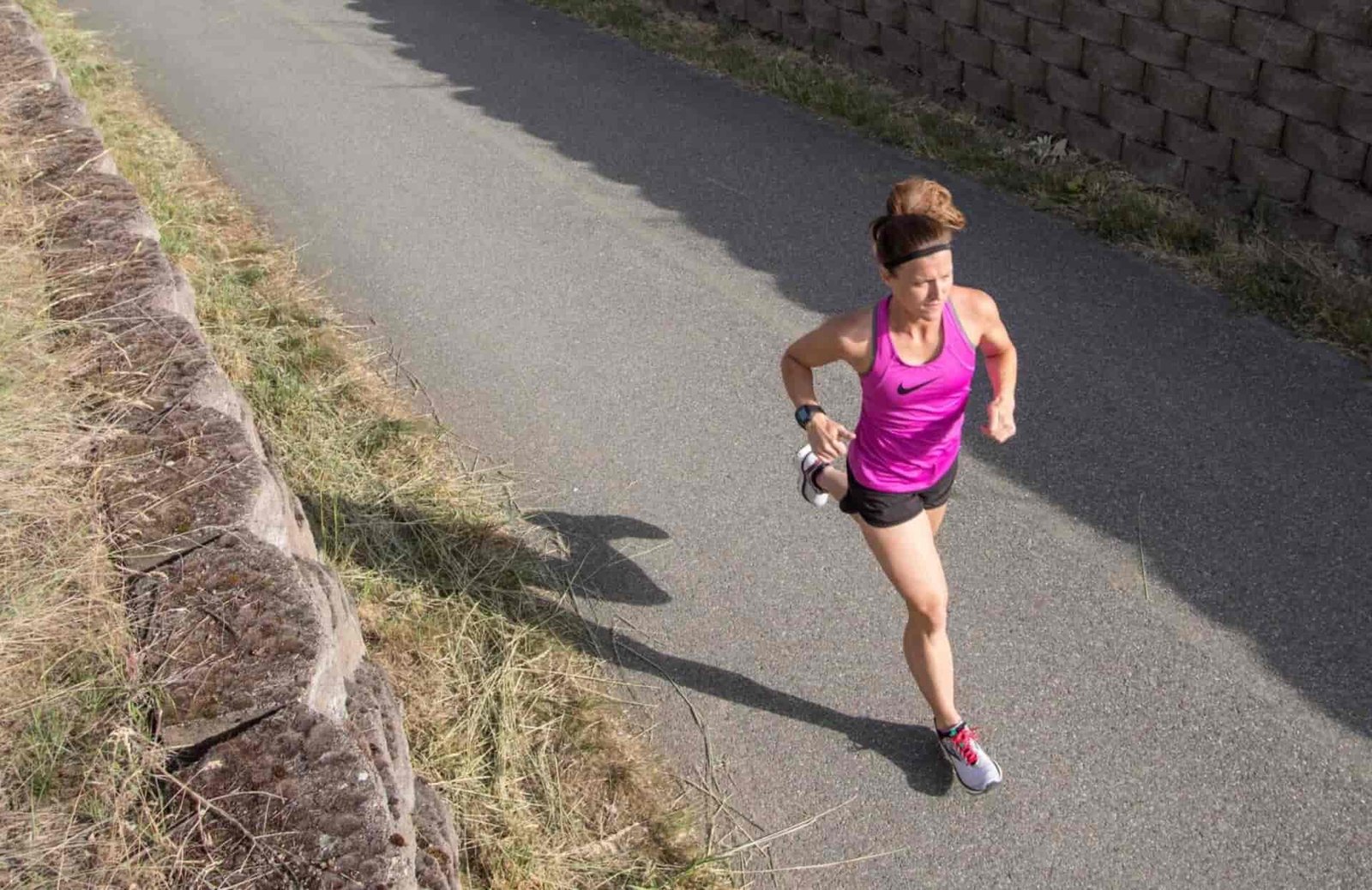 Woman with a purple top running on a paved trail.