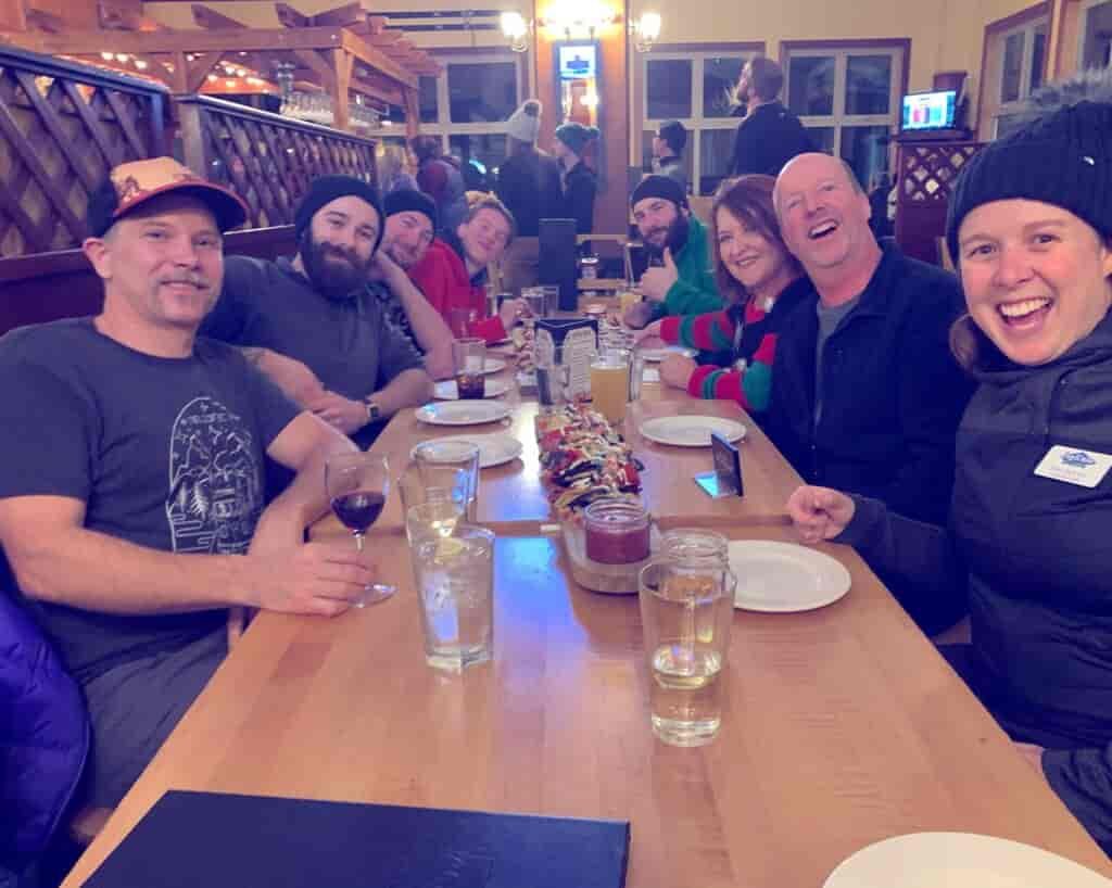 Happy people sitting alongside a long table in the ski lodge during happy hour.