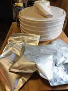 Silver mylar bags of dehydrated meals and a white-colored, circular dehydration machine.
