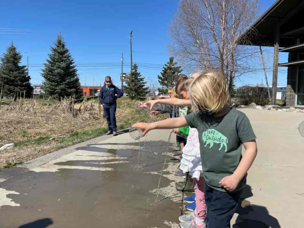 Students pouring water from cups onto the ground while learning at the Spokane County Water Resources Center. Instructor looks on.