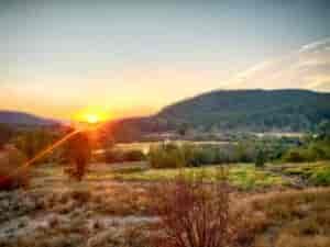 Sunset on the horizon of the hillside with view of the Little Spokane River in the Waikiki Springs natural area. Trees and bushes in the meadow alongside the river.