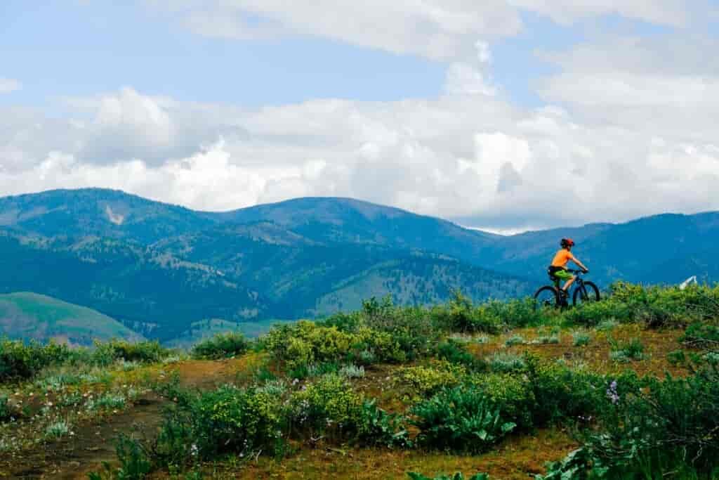 Mountain biker riding along a singletrack trail on a ridge with distance peaks in the background.