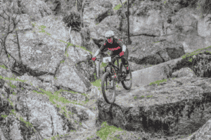 A mountain biker riding on a singletrack trail and over boulders on Beacon Hill.