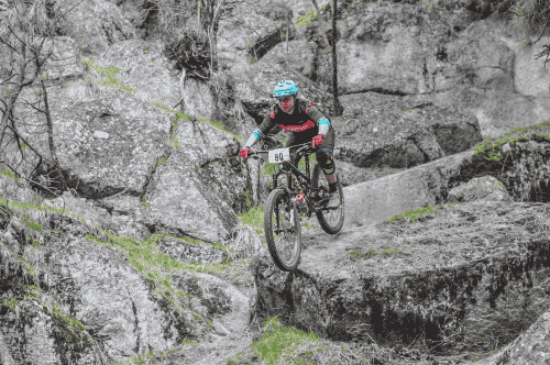 A mountain biker riding on a singletrack trail and over boulders on Beacon Hill.