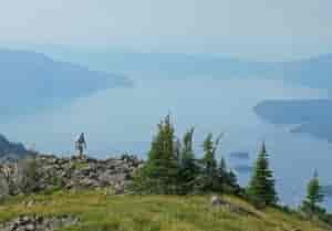 Man running along a rocky dirt trail along a ridge above a lake.