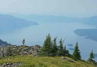 Man running along a rocky dirt trail along a ridge above a lake.