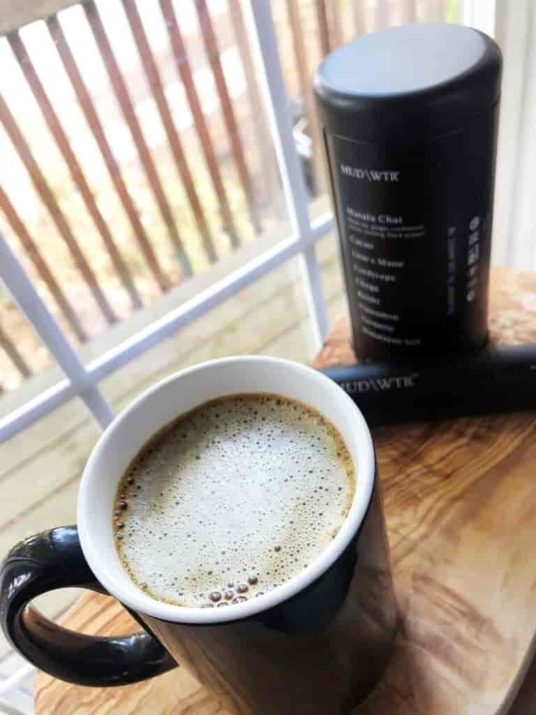 Frothy topped beverage in a mug on a table by a window.