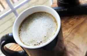 Frothy topped beverage in a mug on a table by a window.