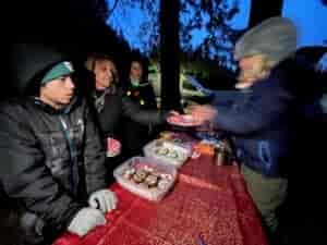 Food buffet line at an outdoor party, with guests dressed in warm jackets, hats, and gloves.