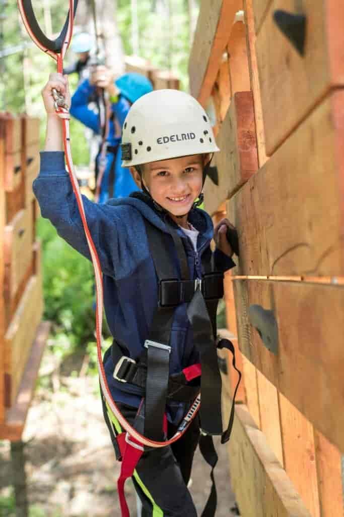 Child wearing a safety harness and helmet smiling at the camera while adventuring in the aerial park at Mica Moon.