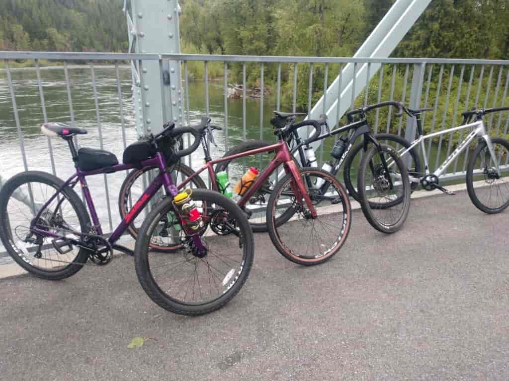 Four bikes standing and leaning against the railing of a bridge over a lake.