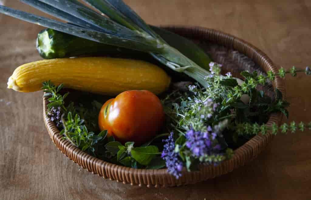 Preserve the fall bounty by canning vegetables: basket of yellow squash, kale, and tomatoe.