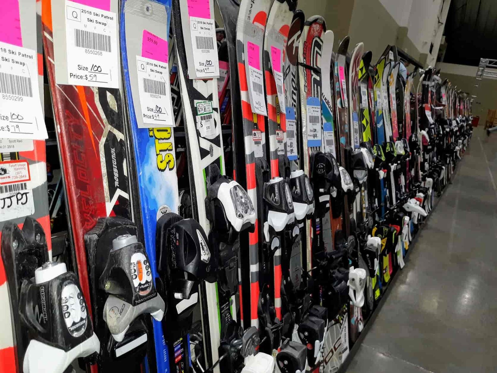 Row of alpine skis, standing against the wall, with sales tags on them.